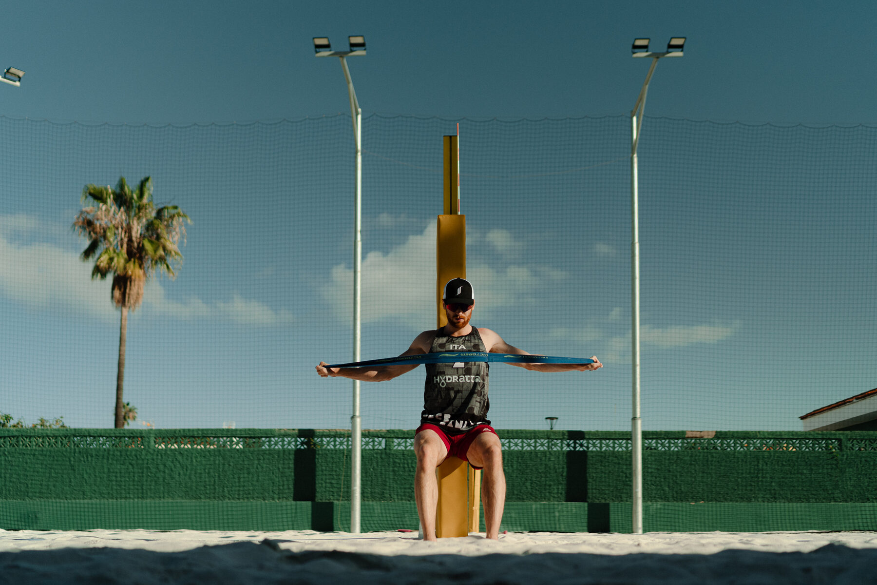 Player stretching with a resistance band beside a palm tree