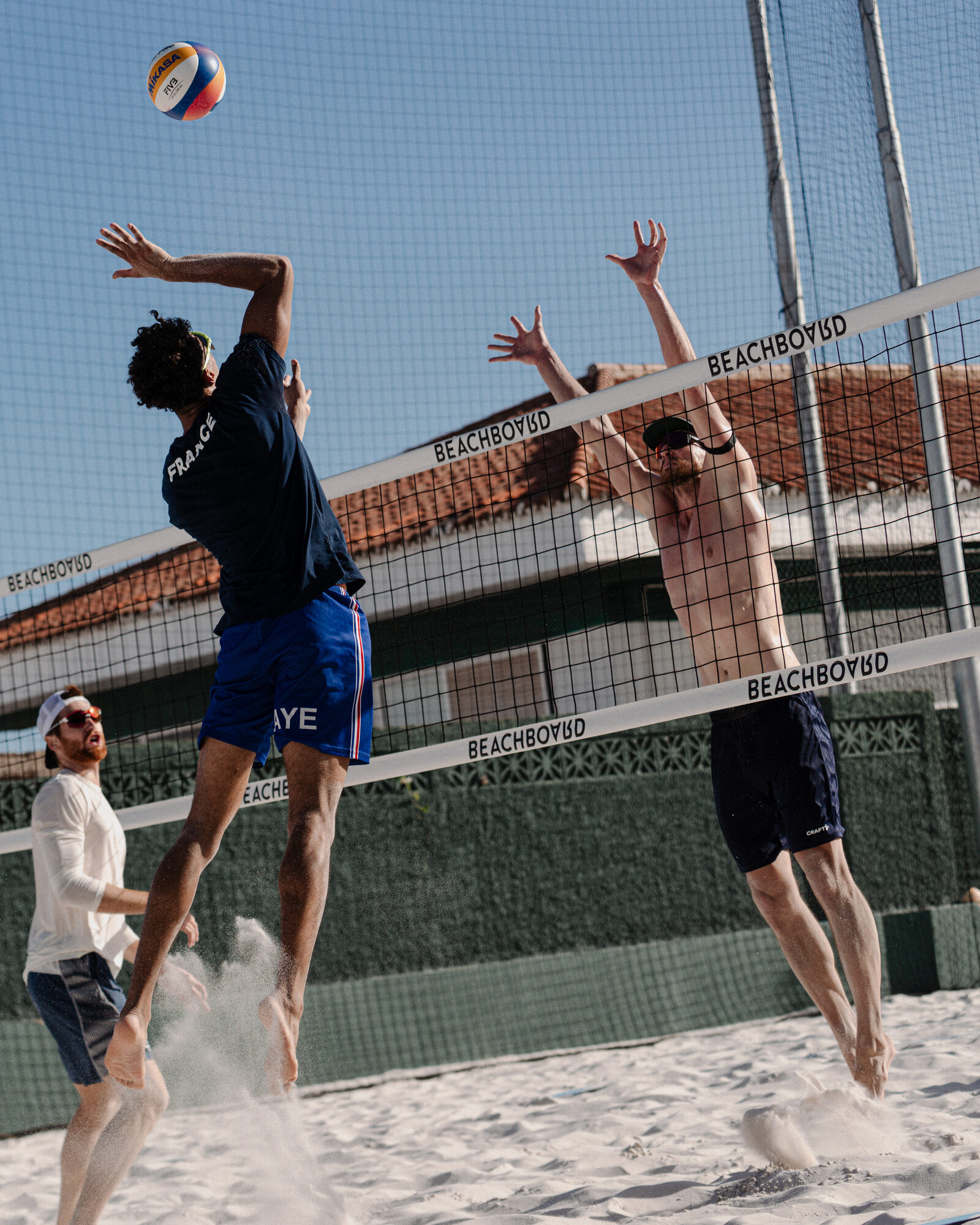 A national-team player attacks against a block, sand flying, on a Hacienda court