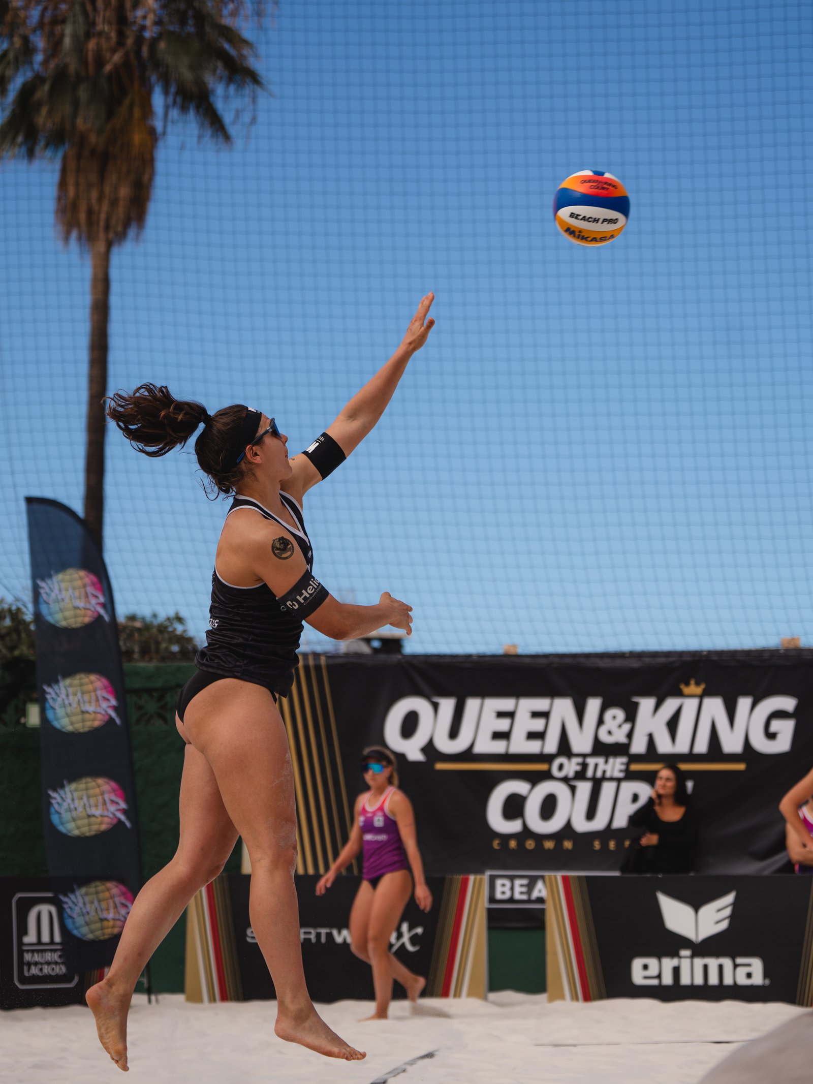 A player reaches up to serve against a Queen and King of the Court backdrop